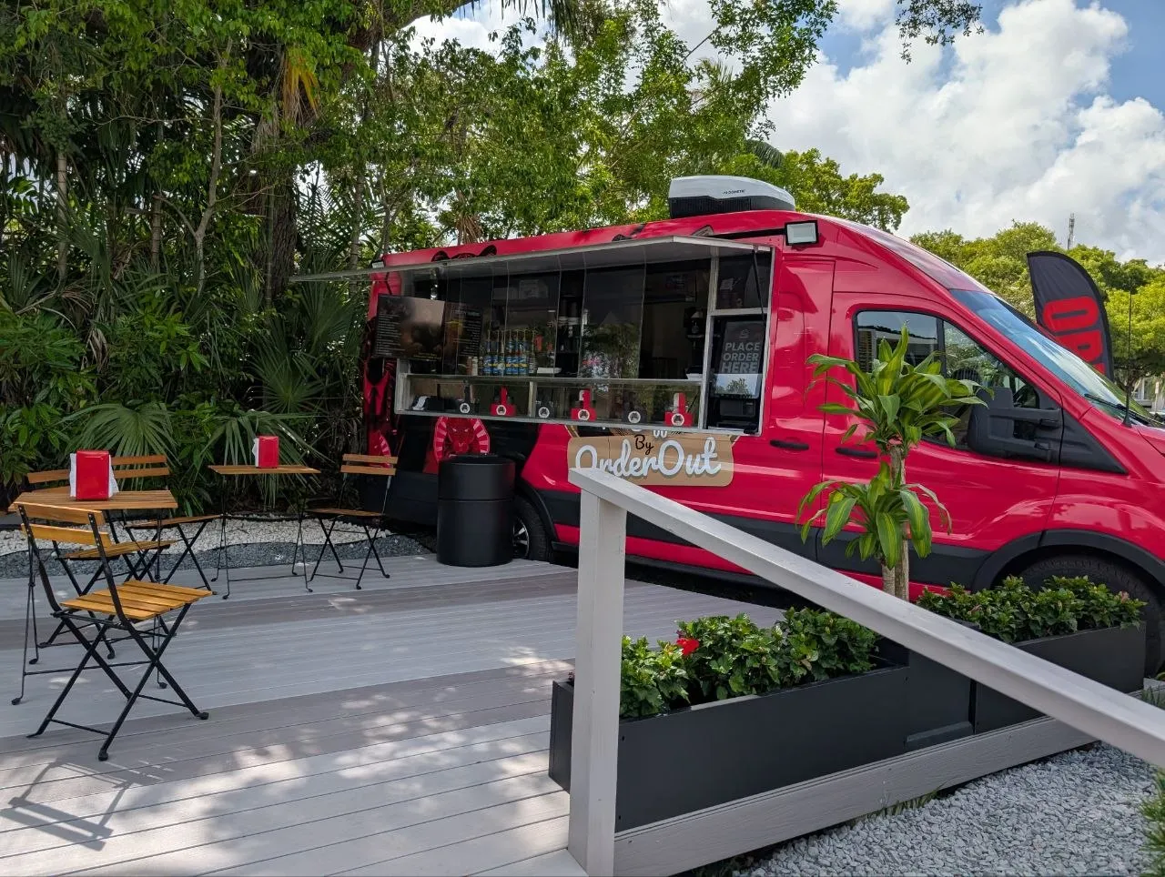 The red OrderOut Bites food truck parked under the trees, with seating out front
